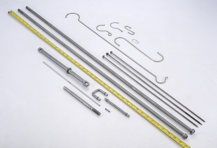 Extra long screws, formed metal rods, and hooks in various lengths and shapes displayed beside a measuring tape